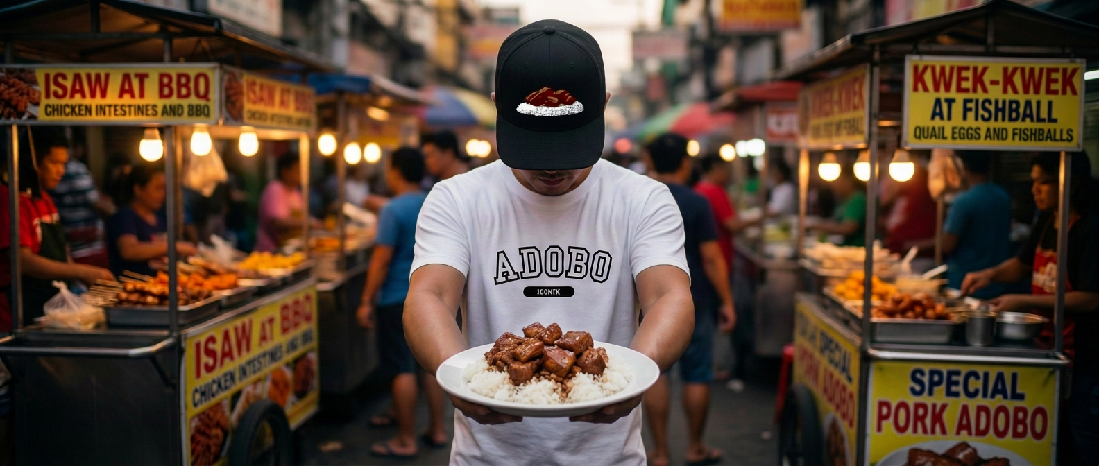 Man wearing a white collegiate Adobo t-shirt and black embroidered snapback hat holding out a plate of fresh pork adobo over rice in a bustling Manila night market.